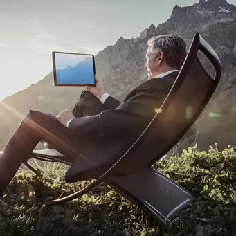 Mann sitzt im Sonnenstuhl und halltet ein Tablet in der Hand